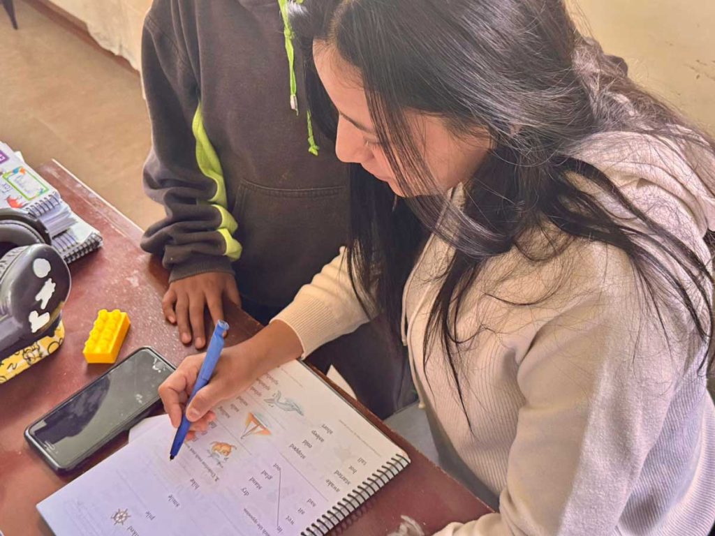 Diana, a sociologist and educator, working one-on-one with a young student on an English phonics workbook at HopeSeed School.